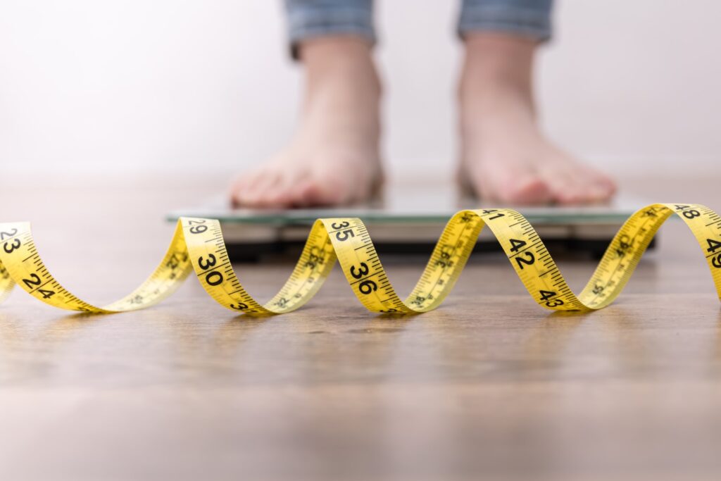 Female leg stepping on weigh scales with measuring tape.