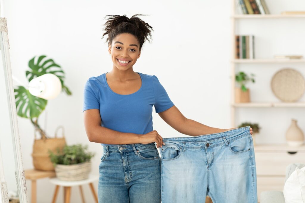 Weight Loss. Happy Slim African-American Girl Showing Old Oversize Jeans After Successful use of Tirzepatide.