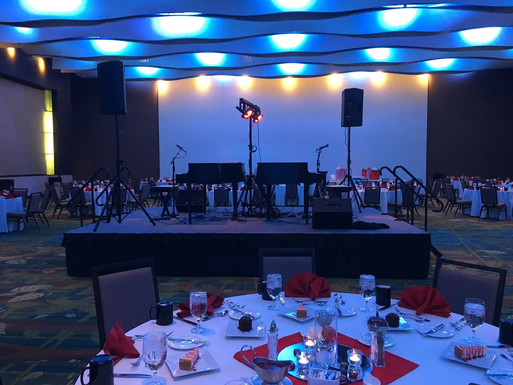 Two pianos, microphones, speakers, and lighting set up in an event ballroom