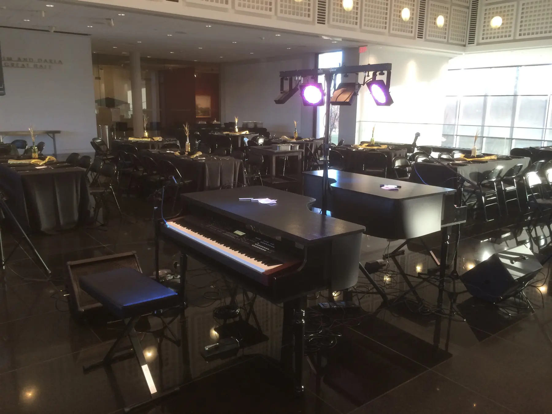 Dueling pianos and sound equipment arranged in a room with round event tables